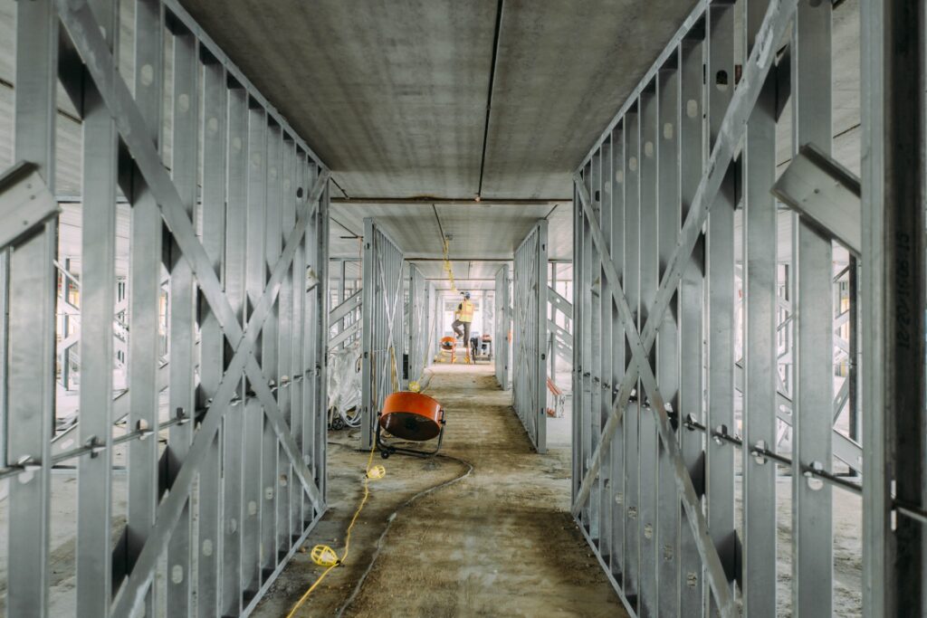 grey metal bar walls during construction of building with electrician working in the distance